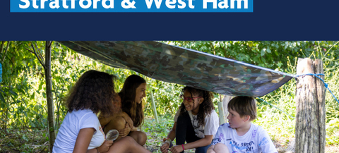 Four children are sitting under a makeshift shelter made of a camouflage tarp in a wooded area. The children have their faces obscured for privacy. They appear to be engaged in conversation or an activity together. Above the image, there is text that reads "People Powered Stratford & West Ham" with the Newham London logo on the right side.