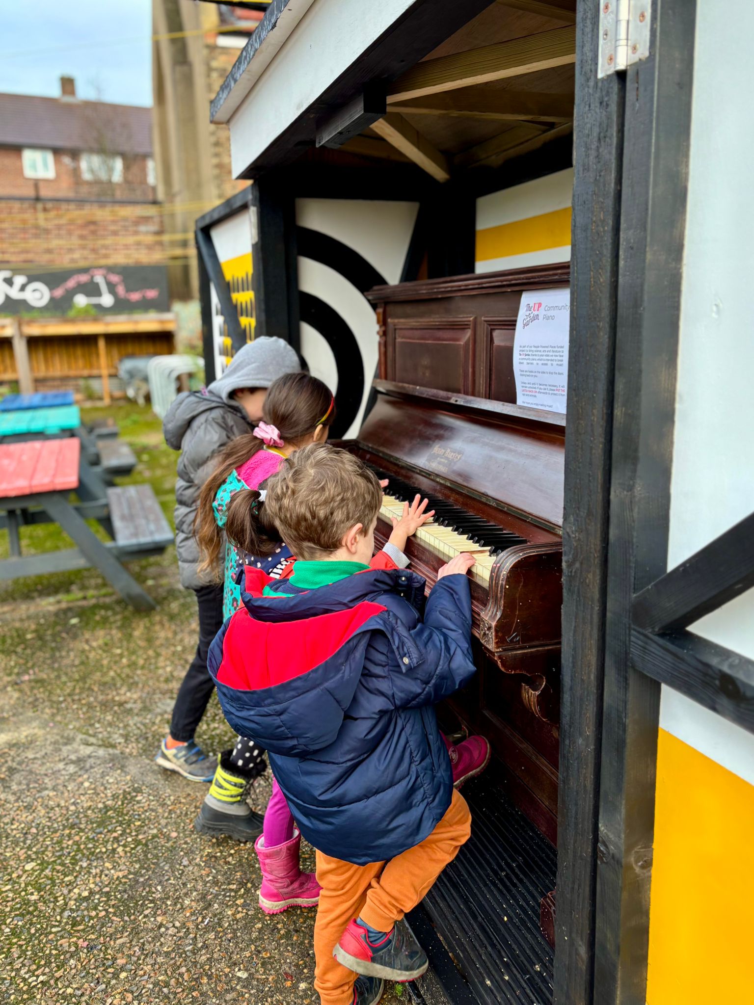 children playing the community piano, with the cabinet doors open to display the internal artwork